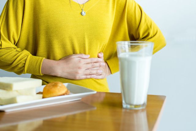 Frau mit Bauchschmerzen neben einem Glas Milch – typische Beschwerden bei Laktoseintoleranz, Abklärung in der Hausarztpraxis Chur West